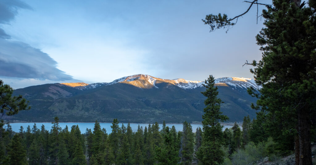 Evening light on snow-striped mountains above Twin Lakes framed by pine trees