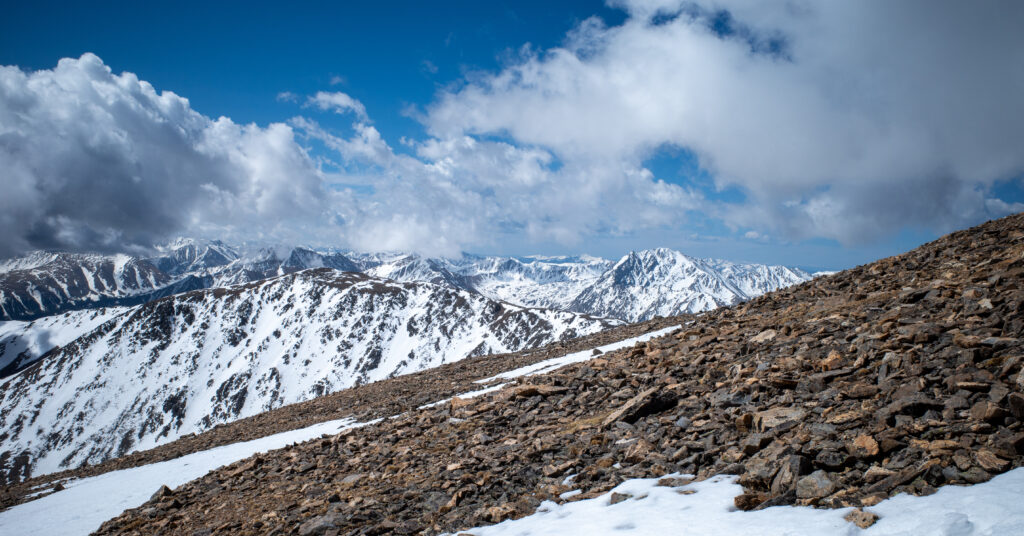 Loose rock and lingering snow on Mount Elbert's upper ridge with snowy Sawatch peaks beyond