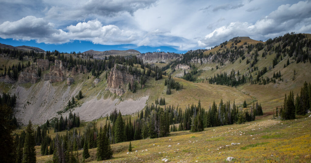 Low clouds above cliffs, meadows, and scattered evergreens along Phillips Pass Trail