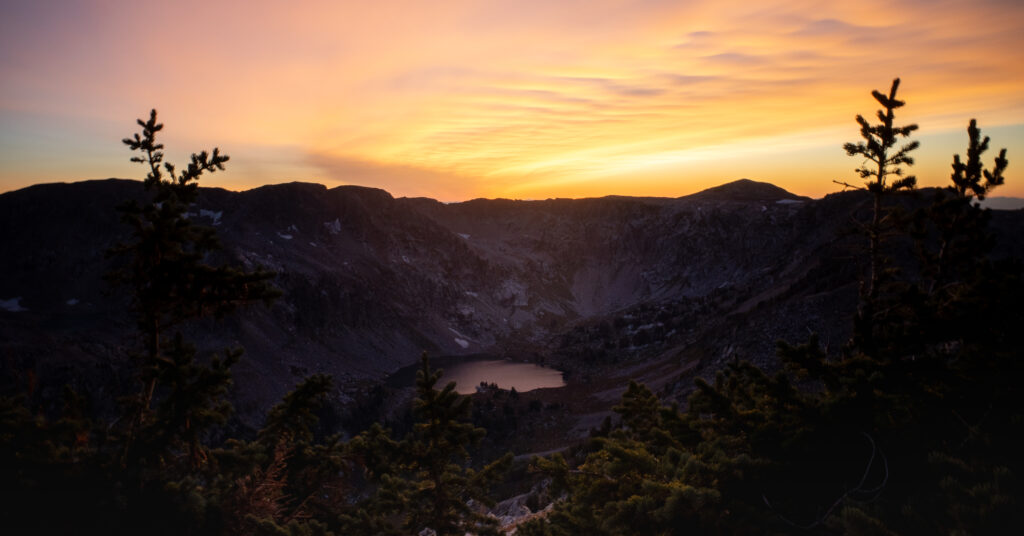 Lake Solitude below a dark ridgeline and orange sunset sky